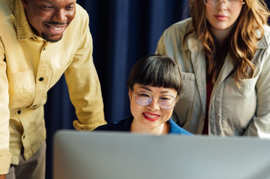 Three colleagues collaborating around a computer, smiling and engaged
